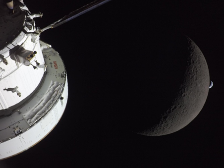Artemis II on lunar flyby with a crescent Moon and a smaller distant celestial body visible against the dark backdrop of space.
